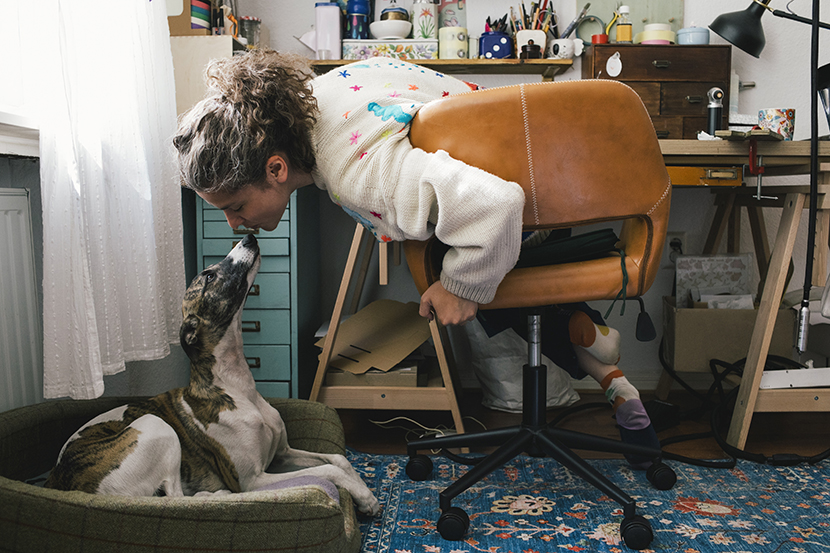 En kvinna som sitter vid ett skrivbord och pussar på en hund som sitter bredvid.